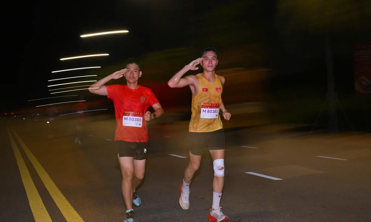 Hai vận động viên cự ly 21km vừa chạy vừa thực hiện động tác chào cờ