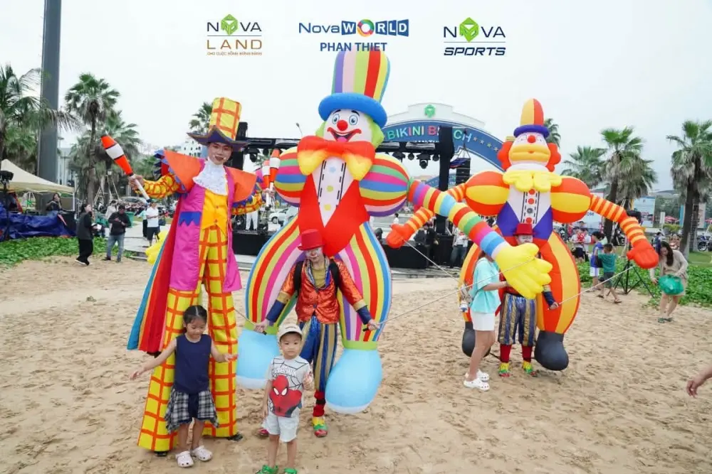 Nghệ sĩ đi cà kheo và ba mascot bơm hơi cỡ lớn chụp ảnh cùng trẻ em trước cổng Bikini Beach