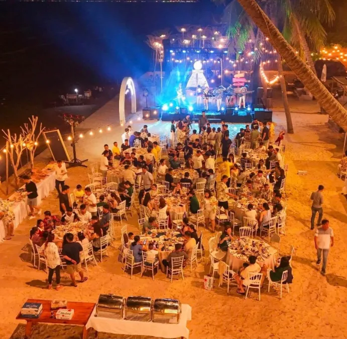 Tiệc gala bãi biển về đêm: sân khấu nhạc sống, bàn buffet, đèn giăng trên cát