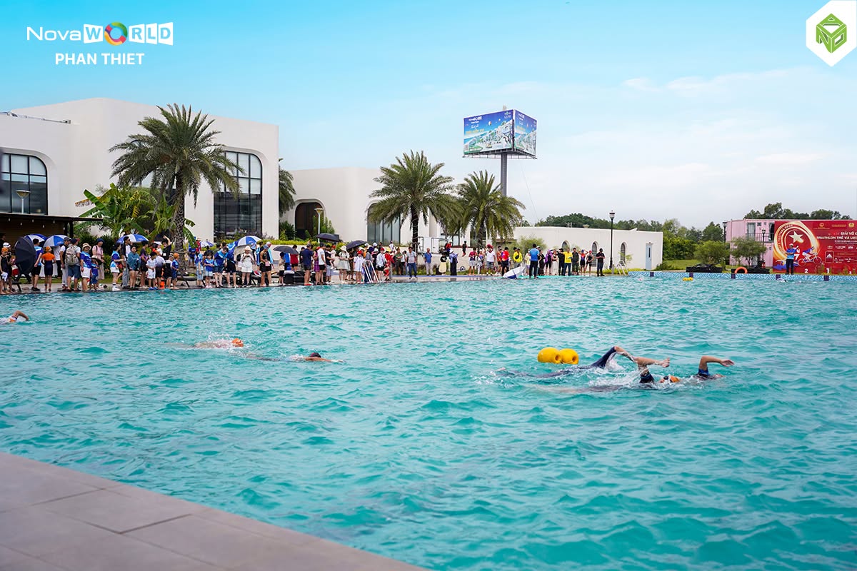 Các vận động viên bơi trong hồ bơi ngoài trời của NovaWorld Phan Thiết, phao vàng đánh dấu đường đua, khán giả đứng dọc mép hồ